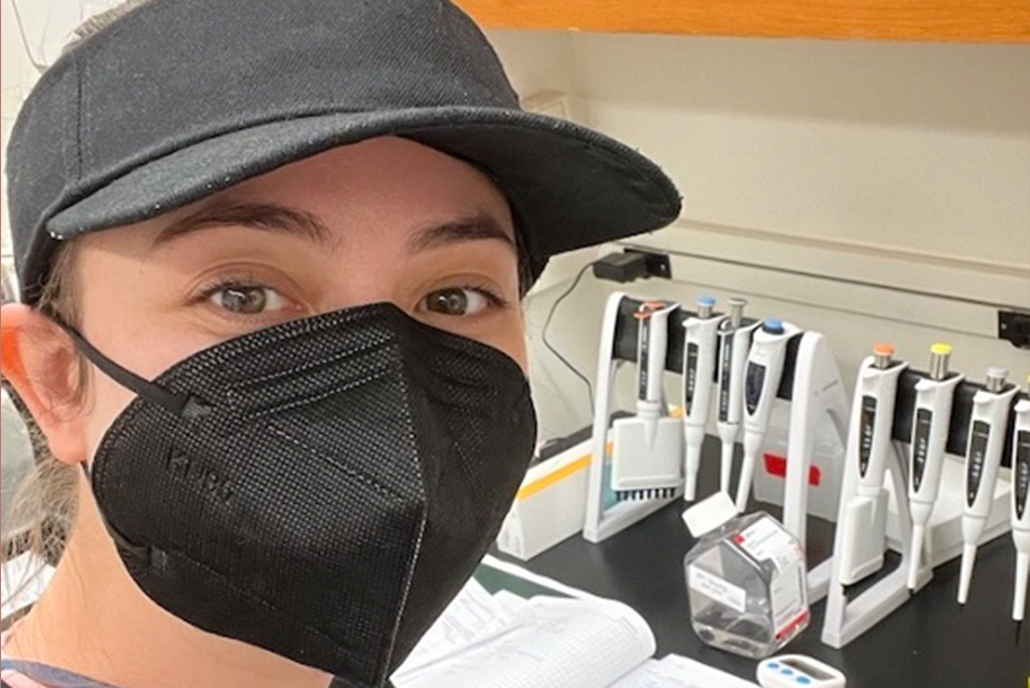 graduate student in a lab with a hat and mask on.