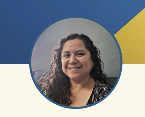 Headshot portrait of a smiling woman with long curly dark hair, shown inside a circular frame. She is wearing a dark patterned top and photographed indoors against a neutral background. The circular portrait sits on a graphic backdrop with a blue and gold diagonal design above and a light cream section below.