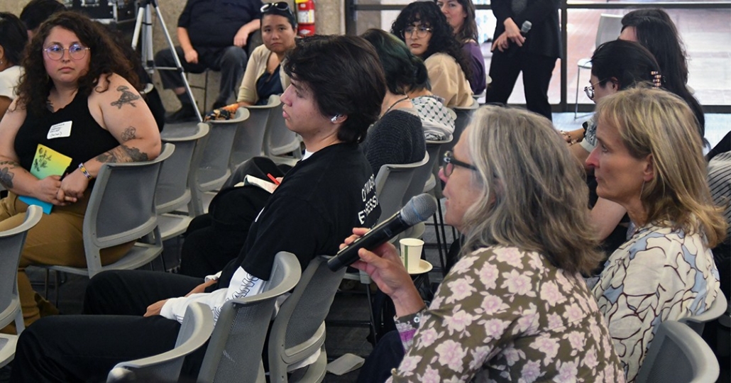 Crowded room of people. One person is holding a microphone.
