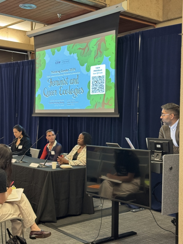Four panelists sit at a table. Above them is the conference screen.