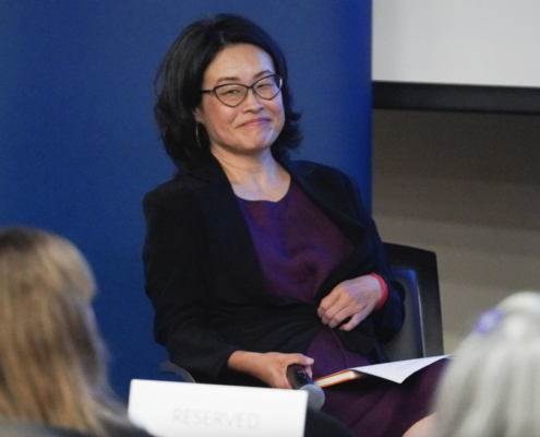 Grace Hong, wearing purple and black clothes and a pair of black glasses, sitting in chair.