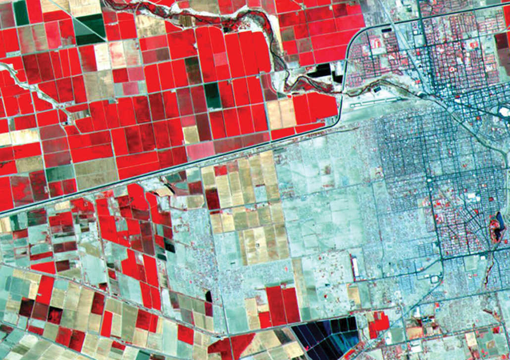Data Border Book Cover False-color satellite image showing a patchwork of rectangular agricultural fields in bright shades of red, dark red, tan, and green on the left, contrasted with a dense gray-blue urban grid on the right. A winding river runs across the upper portion of the image, while straight roads and canals divide the farmland into geometric blocks. The red coloration indicates healthy vegetation in infrared imagery.